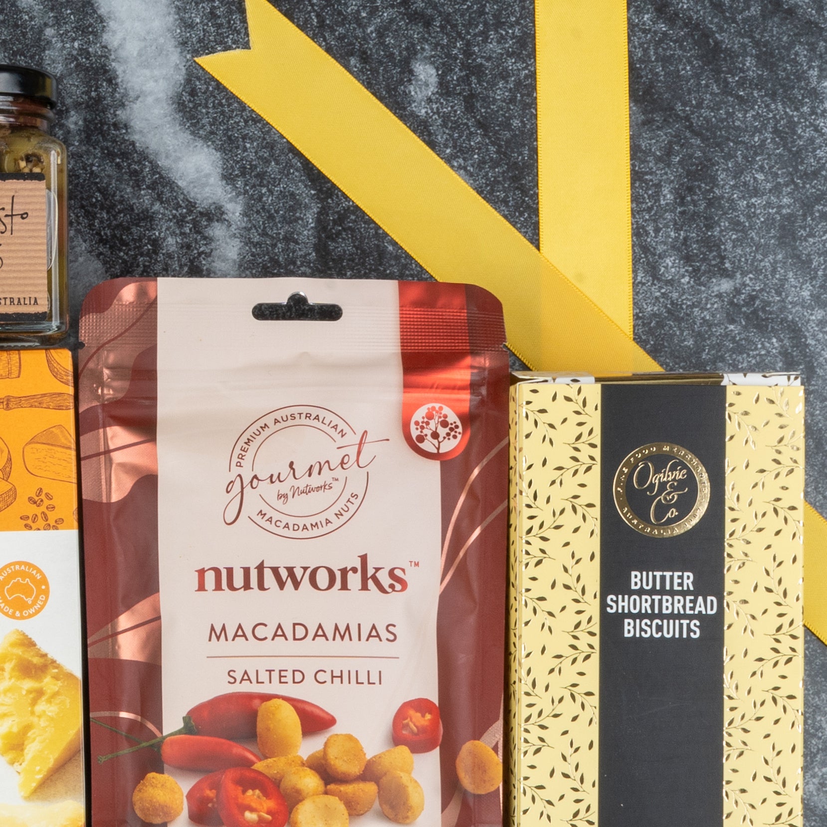 A close-up of The Hamper Boutique Co's White Wine Gourmet Hamper, featuring assorted gourmet snacks and treats on a dark marble surface with yellow decorative accents.