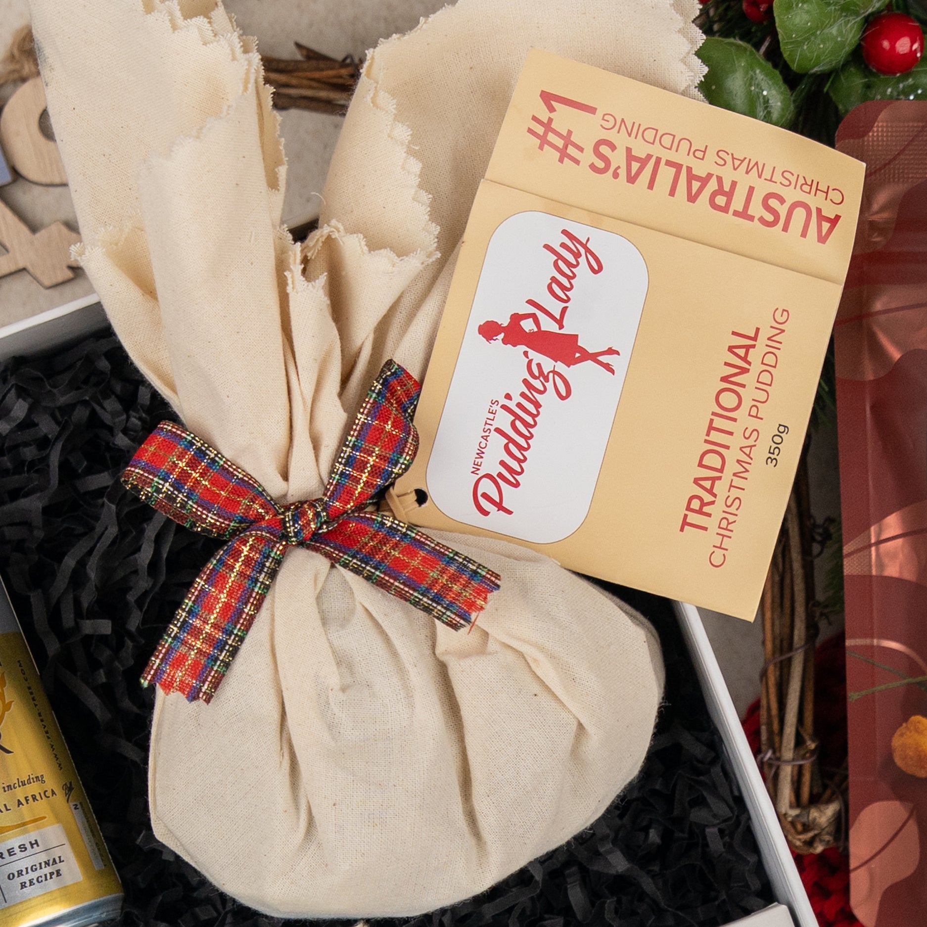 A Cheers & Tonic gift from The Hamper Boutique Co, elegantly wrapped with a festive ribbon and displayed beside a greeting card, presented on shredded black paper.