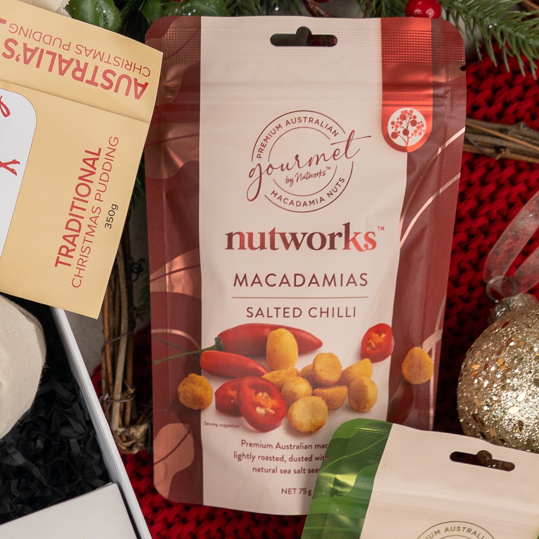 A Cheers & Tonic gift box from The Hamper Boutique Co is displayed on a festive surface, surrounded by holiday-themed items including a box labeled Traditional Christmas Pudding.
