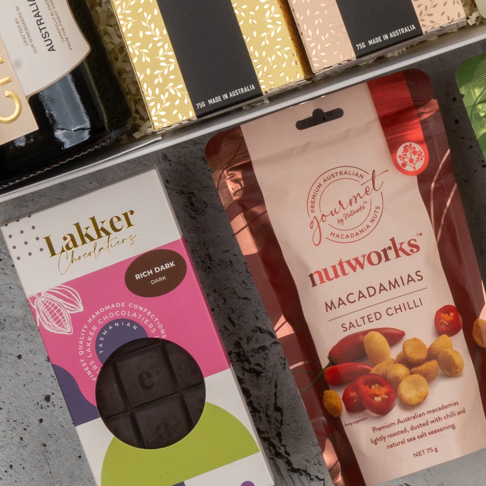 A close-up of The Hamper Boutique Co's Chandon Gourmet Celebration Hamper, showcasing assorted boxed and bagged Australian treats on a gray surface.