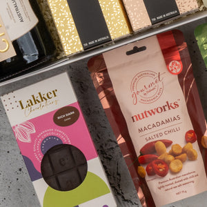 A close-up of The Hamper Boutique Co's Chandon Gourmet Celebration Hamper, showcasing assorted boxed and bagged Australian treats on a gray surface.