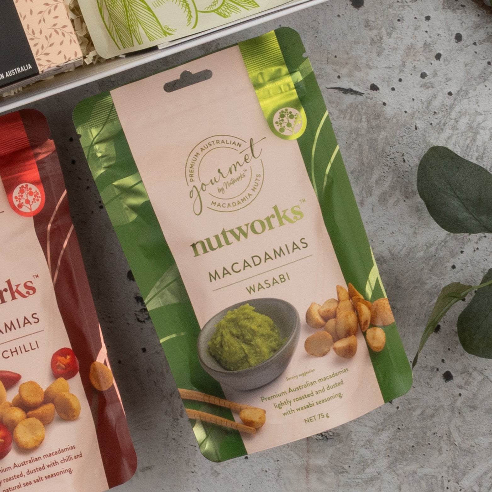 A Chandon Gourmet Celebration Hamper by The Hamper Boutique Co is displayed on a gray surface. The packaging is elegant, and part of another red package appears on the left.