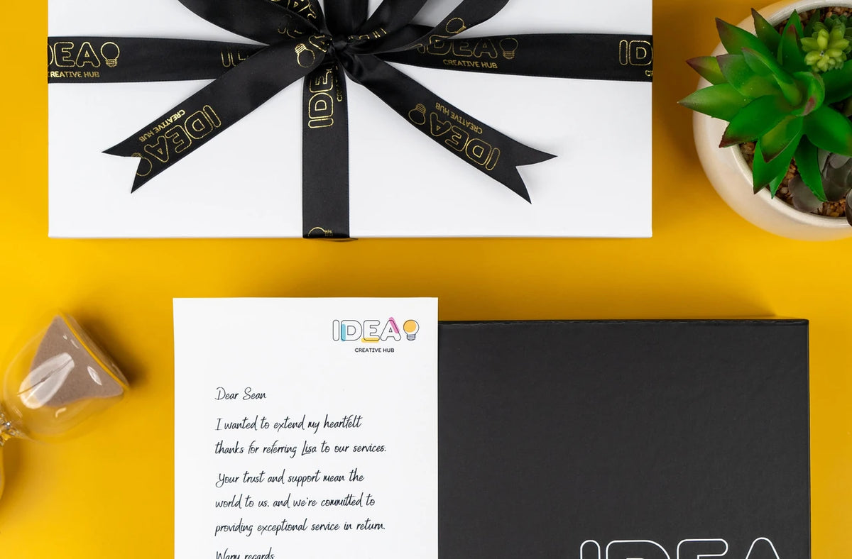 Gift box tied with a ribbon printed with a client’s logo, beside a branded message slip and a branded black box