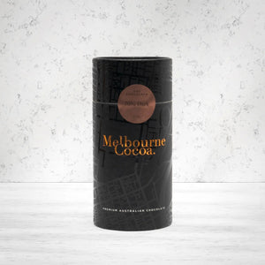 A cylindrical black tin labeled Melbourne Cacao Hot Chocolate 70% Dark 200g by Melbourne Cacao, with gold and copper text, sits on a textured light gray background.