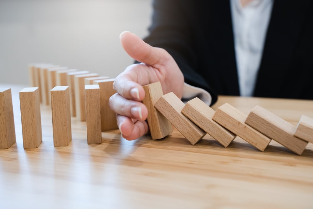 A hand stopping a line of falling wooden dominoes