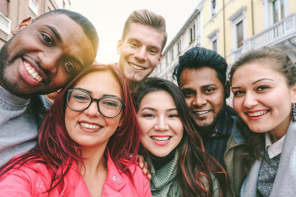 Six smiling young adults standing together on a city street